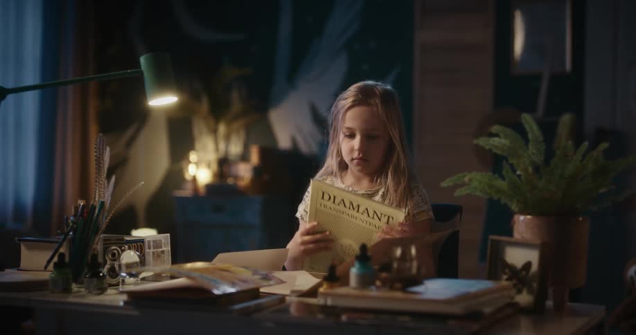 A little blonde girl looking at a book on a table