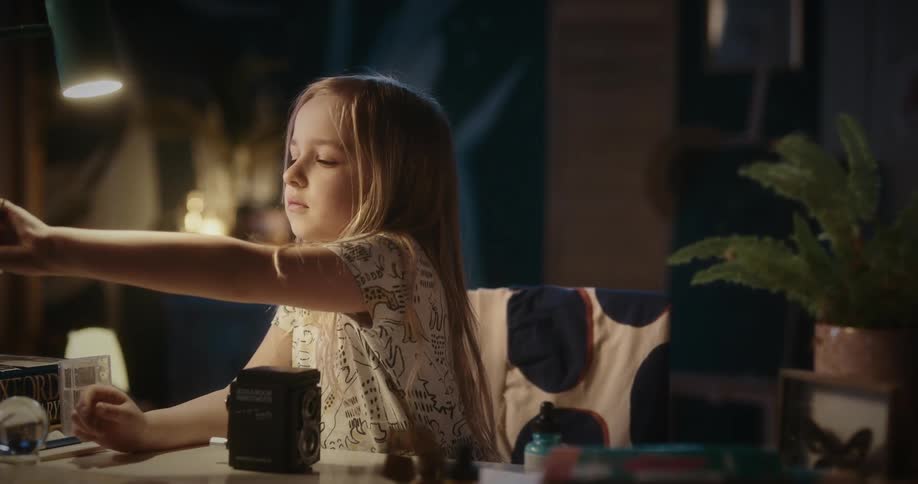Girl sitting picking up a pencil from a table