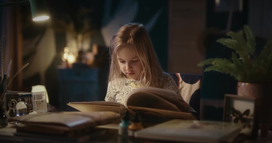 A young girl sits at her desk while concentrating on her reading
