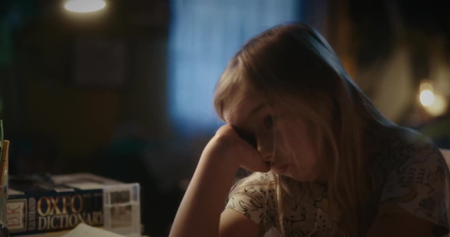Tired and bored blonde girl sits at the table flipping through a book