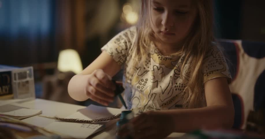 A blonde girl paints by dipping a feather in a paint bottle