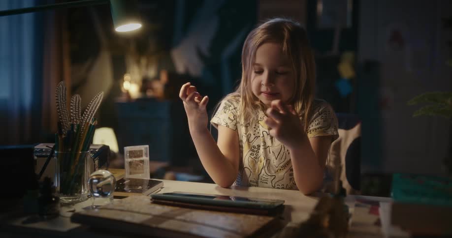 A little girl is sitting at a desk playing with a tablet computer