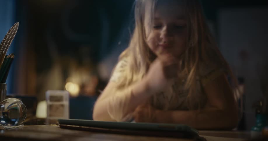A female child operates her tab placed on the table with fingers