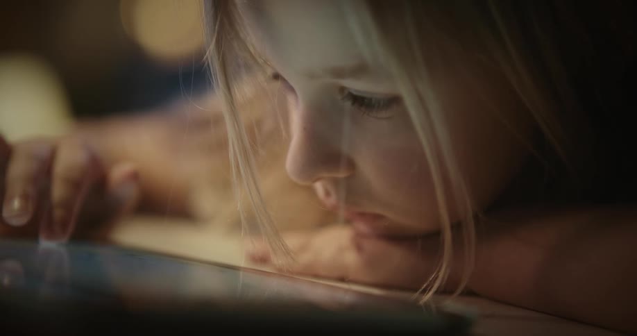 Portrait of a blonde girl typing on a tablet with a bored facial expression