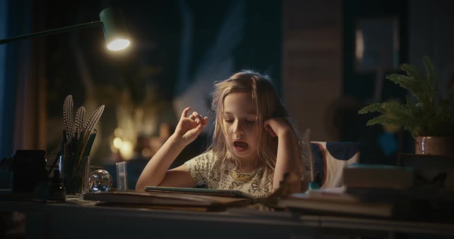 A little girl is sitting at a desk singing as she plays with a tablet computer
