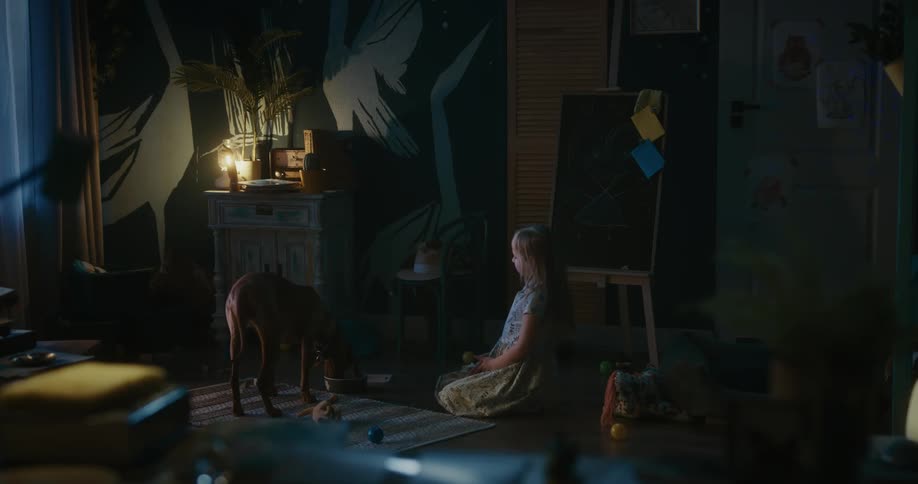 Girl sits on floor in room near easel and pets dog