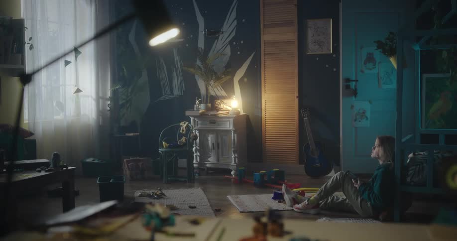 Blonde girl wearing a green hoodie pants and sneakers sits on the floor using a small drone