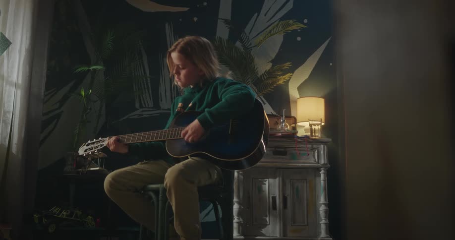 A young boy playing the guitar in the bedroom