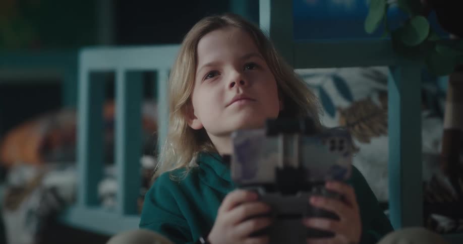 Portrait of a blonde boy sitting and controlling a small drone in an indoor setting at home