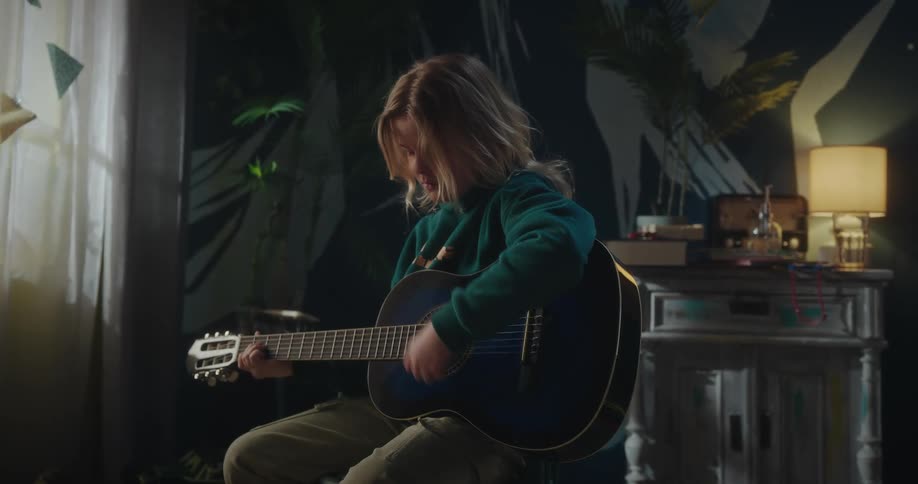 A boy playing the guitar sitting in a room