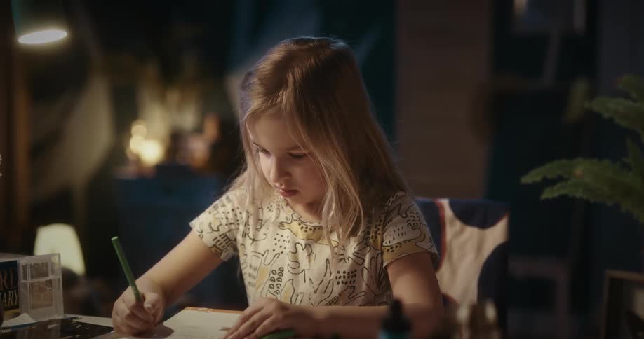 A female child writing on a book with pencil while seated indoor at night