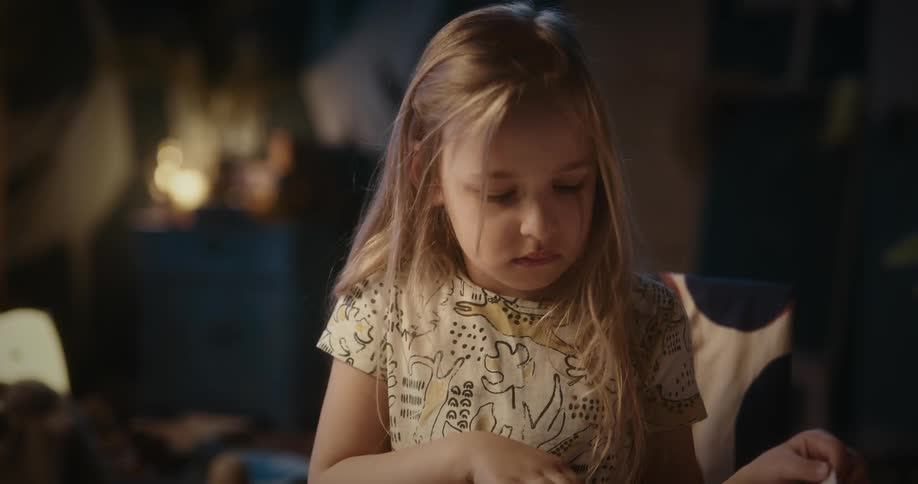 Female child flips book pages while sitting on a chair in a room