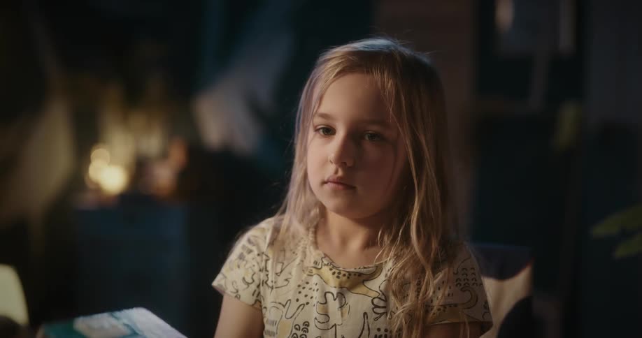A little blonde girl picks up a book to read and makes faces