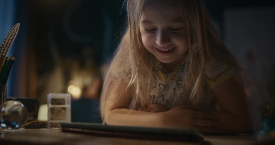 A little girl smiles in excitement while tapping on a tablet