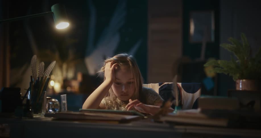 A little girl is sitting at a desk playing with a tablet computer