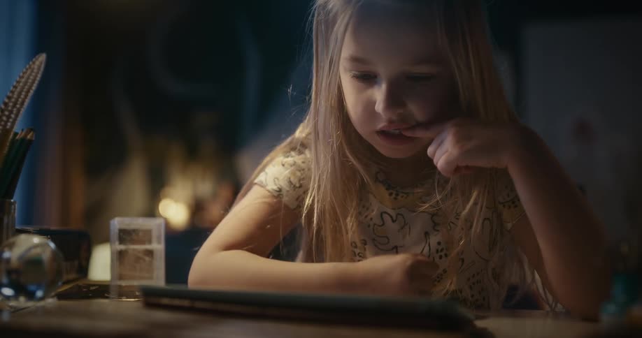 Girl sitting on a dimly lit room playing with a tablet