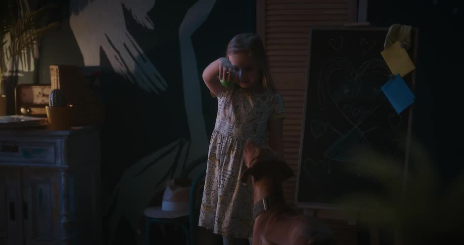 Blonde girl with a beige dress plays ball with brown dog in her room