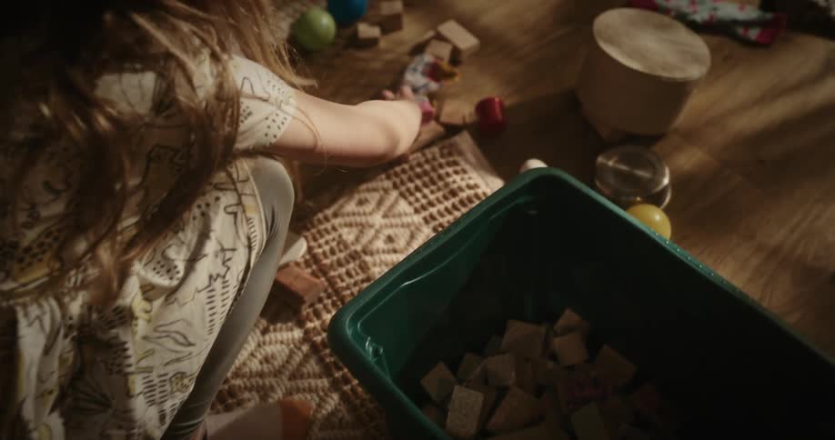 Little girl putting some wooden toy blocks into a box