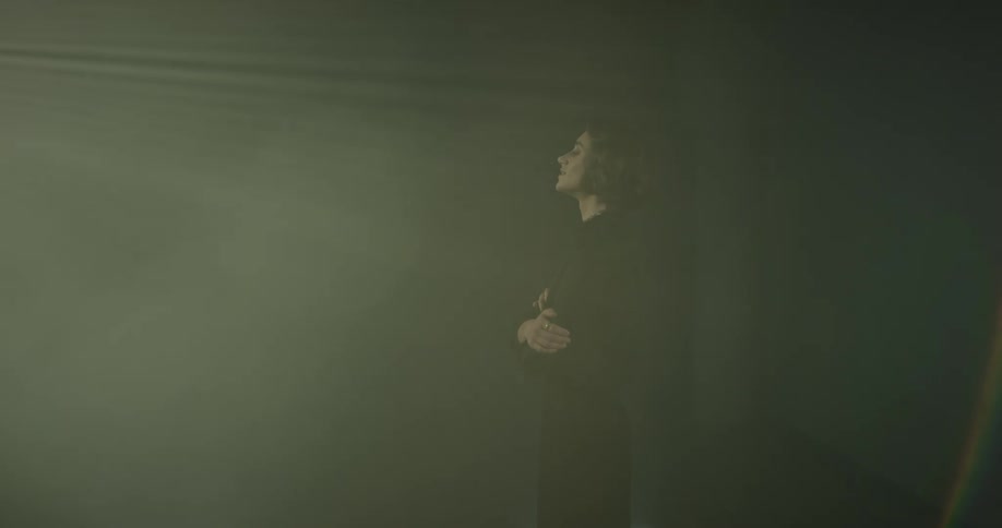 A woman in a dark room standing with her arms crossed