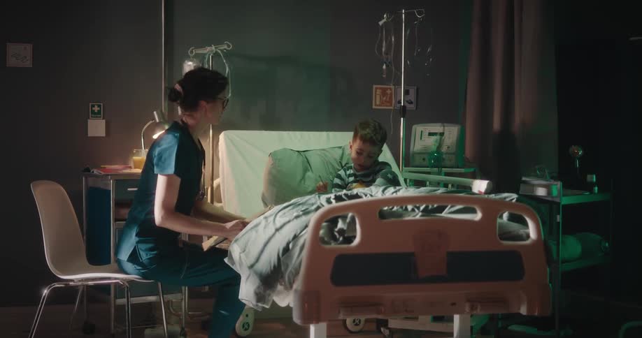 Nurse talking to a boy who is in bed in a hospital room