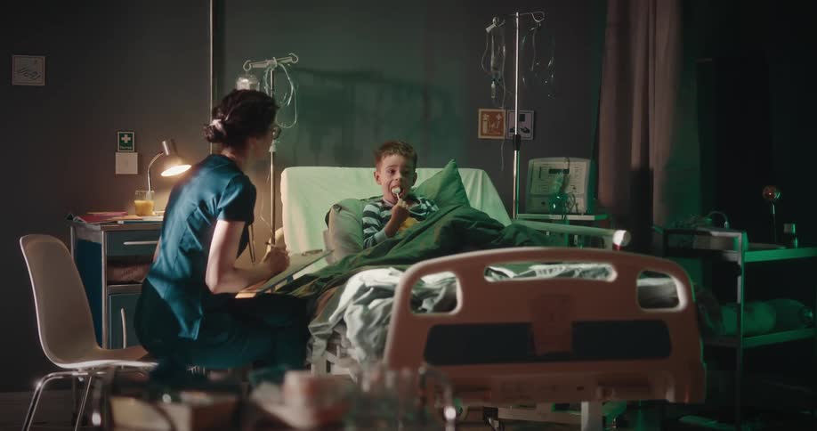 A doctor touches the arm of a little boy to get his attention while making notes in a chart bedside