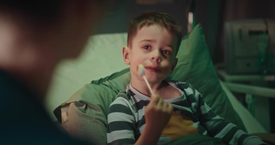 Child patient sitting in hospital bed and eating lollipop coughs