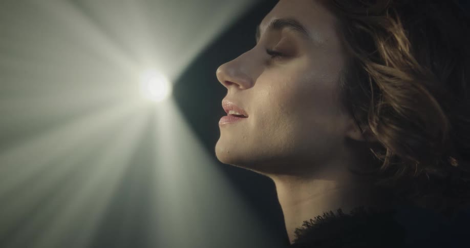 A woman makes sentimental expressions while a bright light behind her illuminates the room