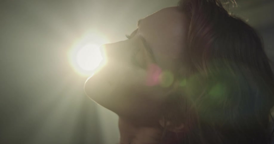 A woman points her face upwards towards a bright spotlight