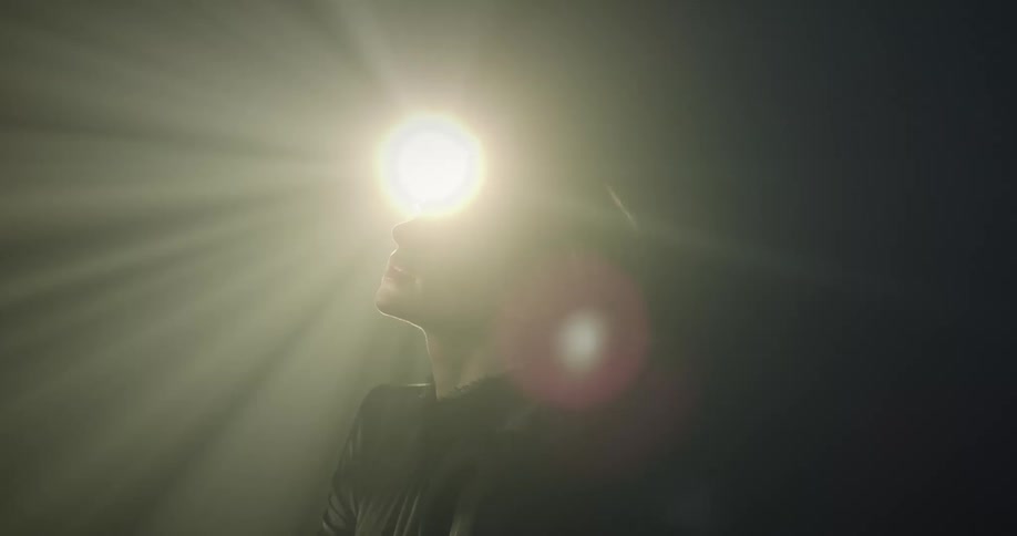Woman in a dark environment with lights reflecting on her face and a happy facial expression