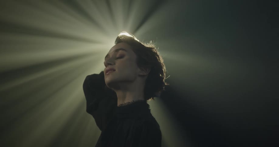 A woman makes expressions of comfort while a light behind her illuminates her