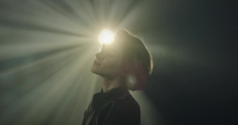 Woman standing in an indoor room with closed eyes and a facial expression of happiness with reflections of light on her face