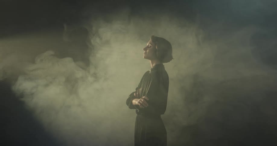 A woman in a dark room with beams of light and fog
