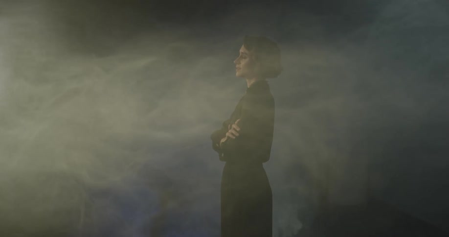 A woman stands in a room that has fog billowing around it