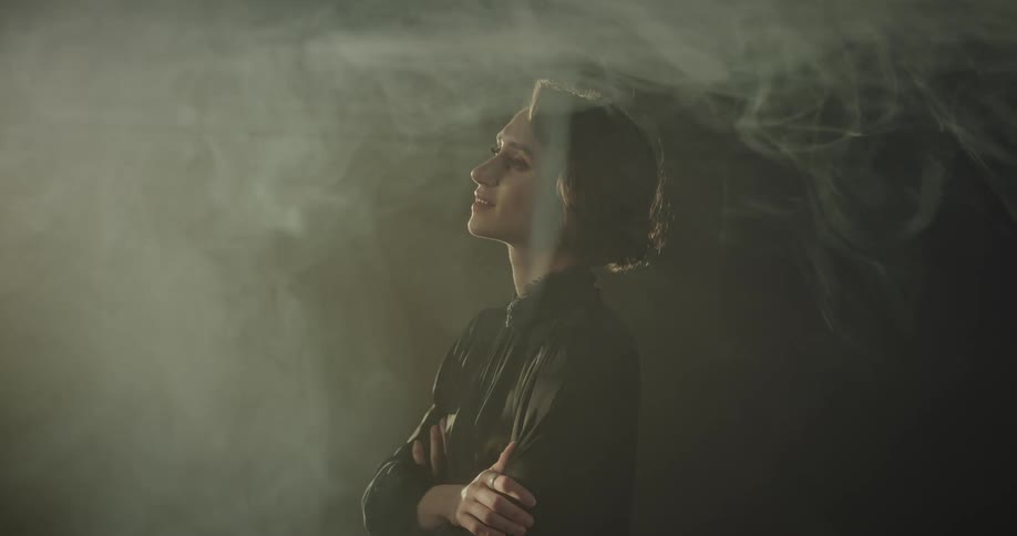 A woman stands with arms crossed and smiles as a light passes by her