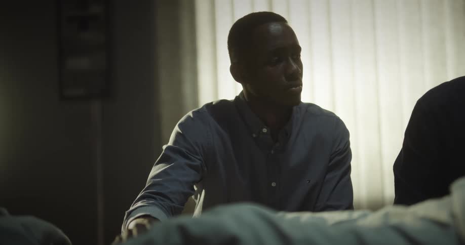 Portrait of two men sitting next to a person lying in bed with a sad facial expression