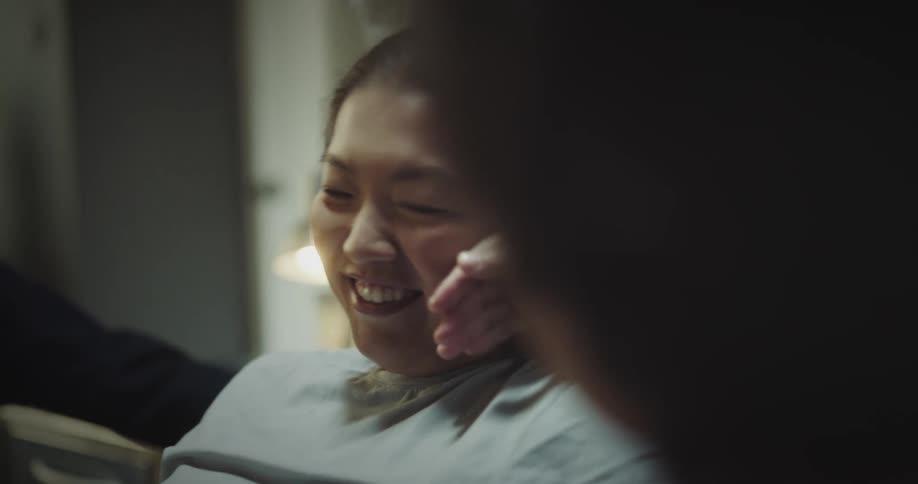 A young asian woman sits in a hospital bed while smiling and laughing with her parents
