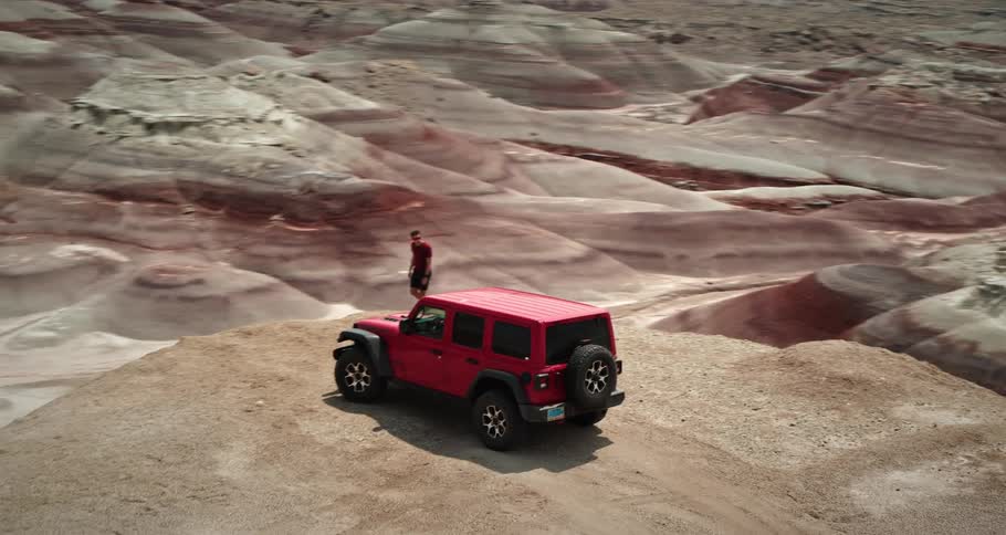 A man walks along a cliff overlooking a wide desert canyon
