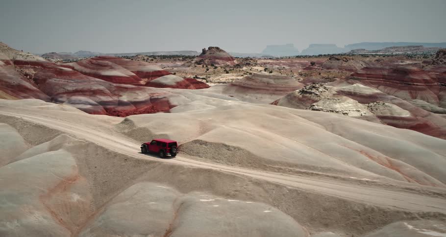 A red van travels on a road through the desert with rock layered mountains and mountain plateaus on the horizon