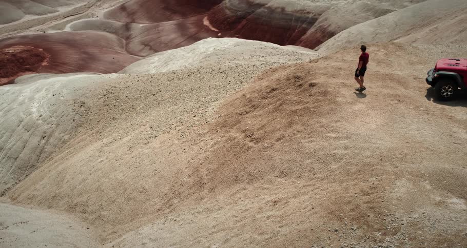 Man walking on a sandy hill next to a red suv in a desert landscape