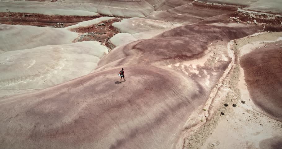 A man is hiking across a rock layered mountain with steep slopes and desert valleys