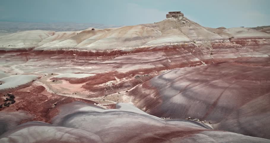 A man is hiking in rock layered mountains with mountains on the horizon