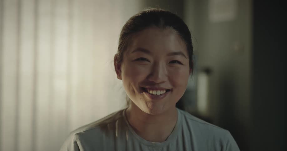 Woman standing in room looks up and grins widely