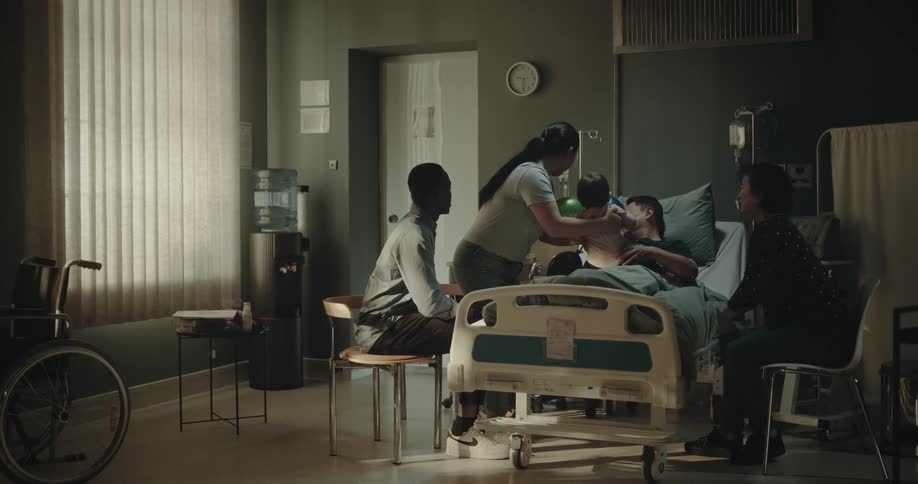 Family around a patient lying in the hospital conversing with a baby