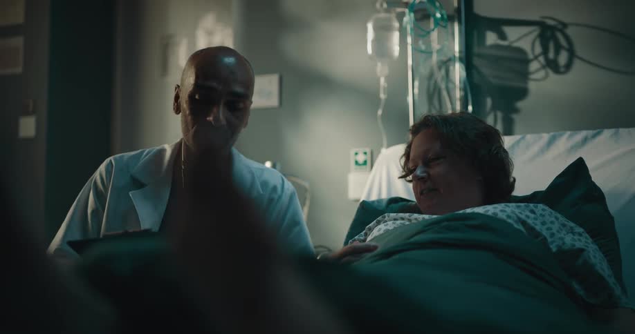 Doctor sitting next to a woman lying in a hospital bed and asking for the patients signature