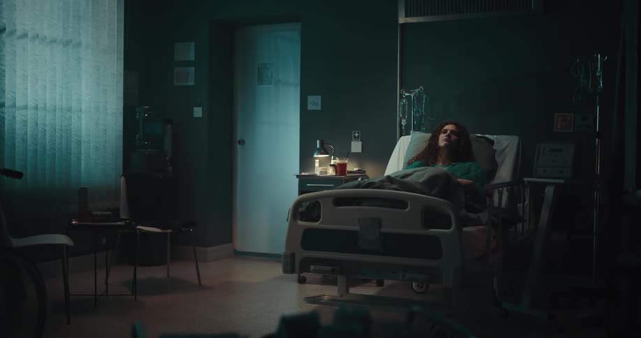 Bored female patient with curly hair lies in hospital bed at night