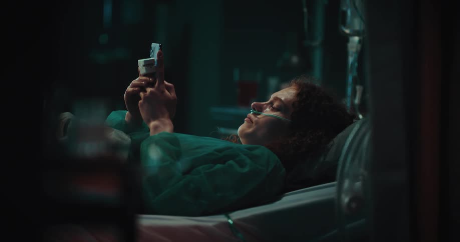 Patient wearing nasal oxygen tube uses tablet while lying down in hospital bed