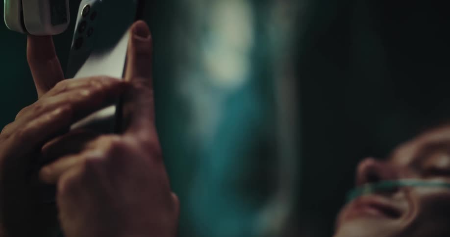A woman is lying in a hospital bed and has a tube in her nose and is using a cell phone
