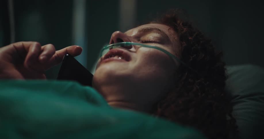 Patient wearing oxygen tube and lying in hospital bed cries during a phone call