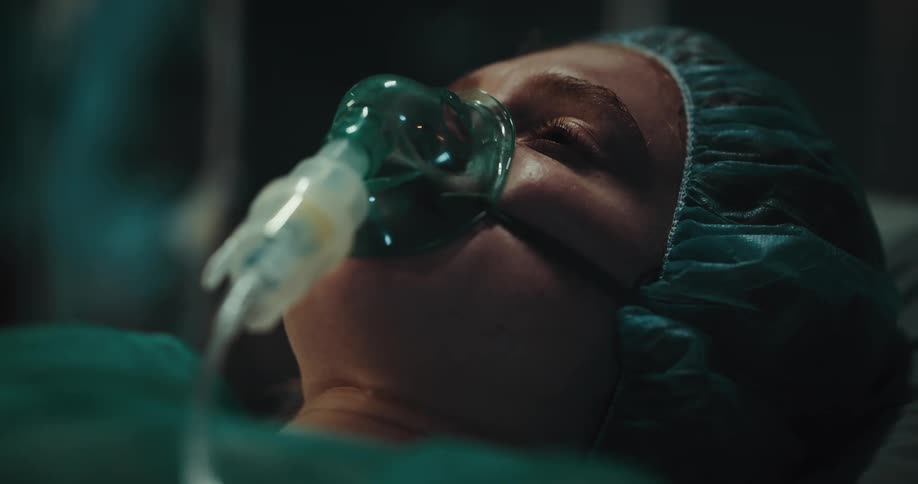 A woman is lying in a hospital bed with a respirator in her nose and mouth