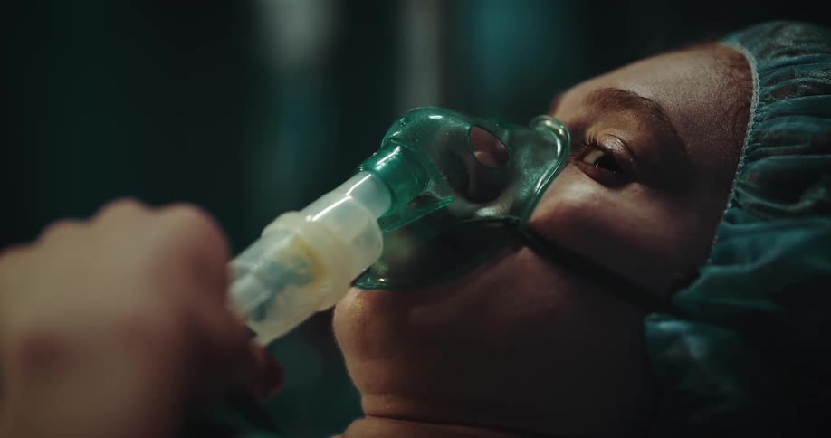 Portrait of a woman in the hospital frightened with an oxygen mask and then calming down